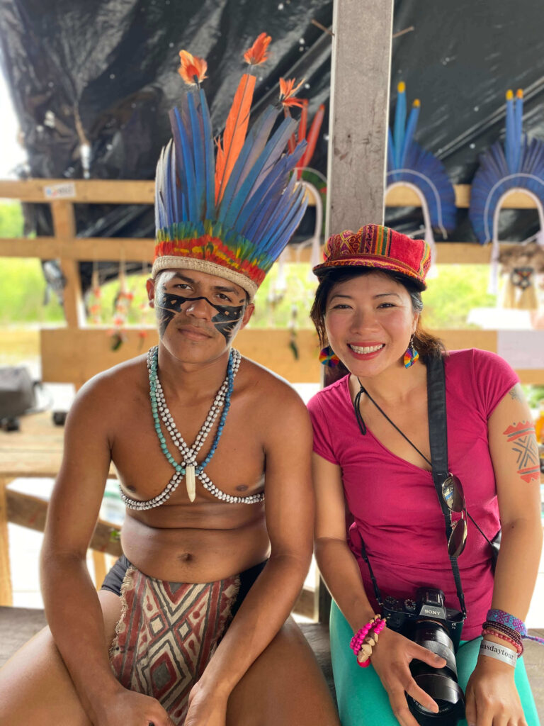 Asian female author sitting beside an indigenous tribal man in traditional outfit in the Amazon rainforest, Brazil