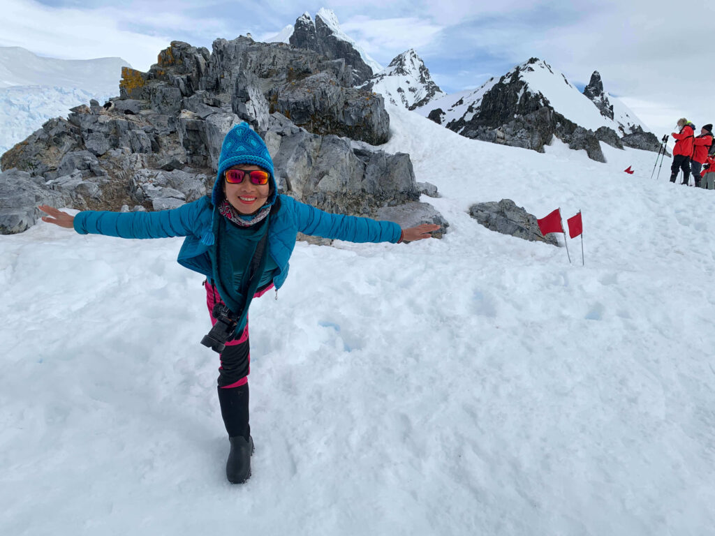Asian female author performing yoga airplane pose on snow in Antarctica, celebrating travel to all 7 continents in her 30s