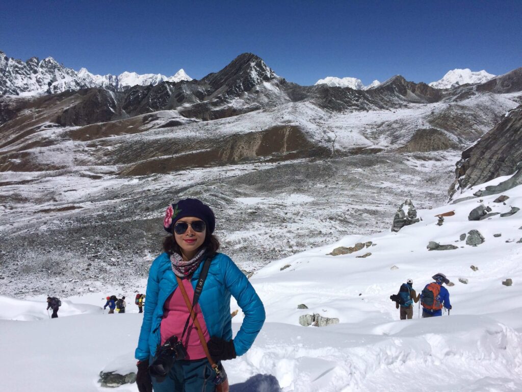 Asian female author standing at Everest Base Camp snowy Himalayan peaks in the background