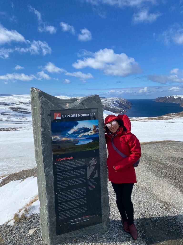 Portrait of a woman at North Cape, Norway, bundled up against the cold with the Arctic Ocean and dramatic cliffs stretching behind her