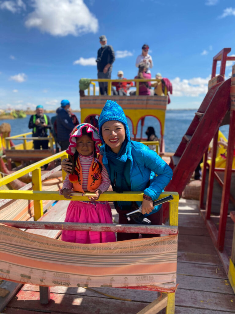 Portrait of a woman traveler with a local girl at Lake Titicaca, Peru, both smiling against a backdrop of traditional reed islands and water